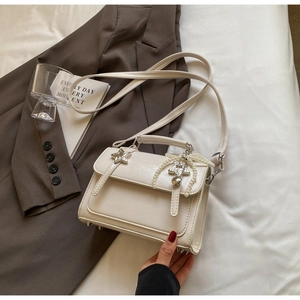 Détail du sac crème avec pendentif perle en nœud et boucles d'oreilles étoile