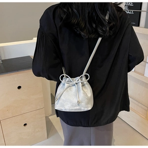 Détail du sac seau argenté à cordon avec décoration de nœud sur fond noir