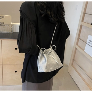Détail d'un sac seau argenté orné d'un grand nœud décoratif et d'une bandoulière fine