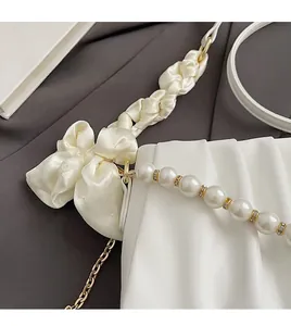 Detailed close-up of pleated white handbag with pearl chain and silk bow strap