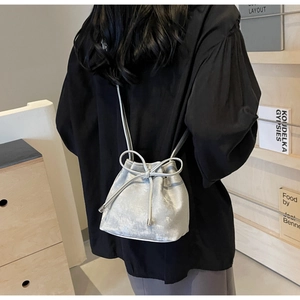 Détail d'un sac seau argenté avec fermeture à cordon et nœud décoratif sur une femme