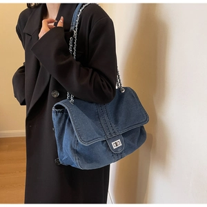 Détail du tissu denim bleu marine avec chaîne argentée et fermoir rotatif en métal