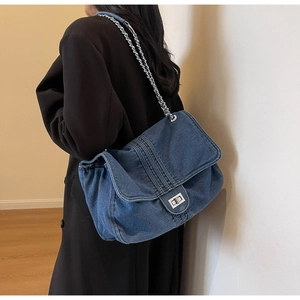 Detailed macro view of denim tote bag showing silver metal chain strap and turn-lock closure