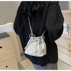 Sac seau argenté avec cordon et nœud porté à l'épaule sur un fond de bibliothèque