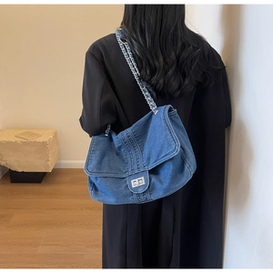 Detail of blue denim shoulder bag featuring silver twist lock and chain strap on a model