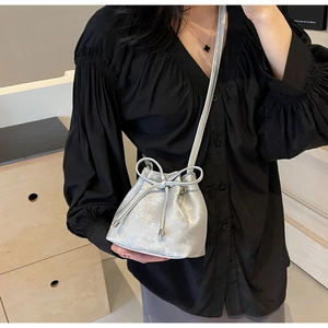 Détail d'un sac seau métallisé argenté avec nœud papillon sur tenue plissée noire