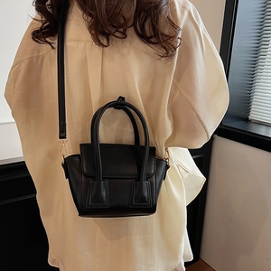 Elegant black leather bucket bag with gold hardware worn as a crossbody shoulder bag