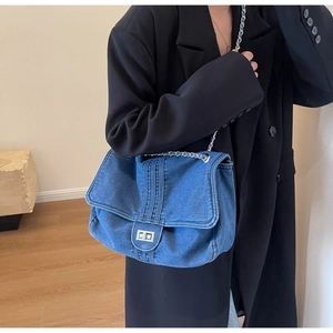 Close-up of denim shoulder bag with silver turn-lock clasp and woven chain strap