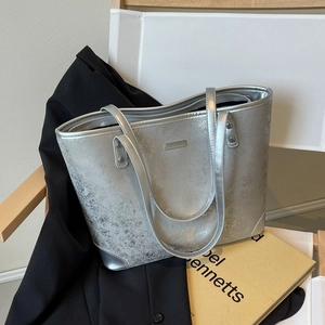 Chic silver metallic tote bag with cracked texture and metal corner details on a chair