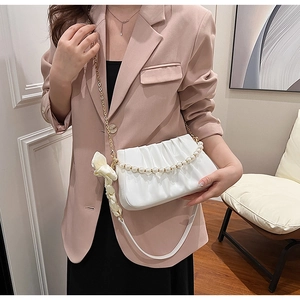 Detail of white pleated handbag featuring elegant pearl chain and silk bow accent
