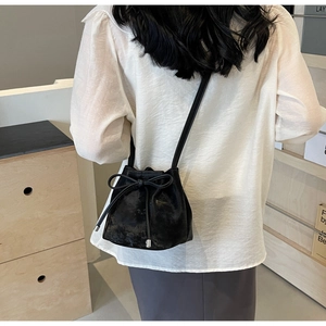 Détail d'un sac seau noir avec cordon de serrage et nœud porté en bandoulière par le modèle