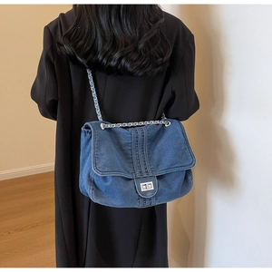 Detail of blue denim shoulder bag featuring silver twist lock and chain strap on model