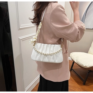 Detail of white pleated underarm bag with pearl chain and silk ribbon shoulder strap