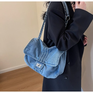 Detail of blue denim tote bag with silver chain strap and metal turn-lock closure