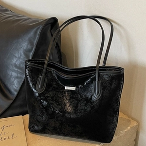 Large black tote bag with cracked leather texture and silver logo on stone surface