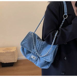 Detail of blue denim shoulder bag featuring silver chain strap and metal turn-lock buckle