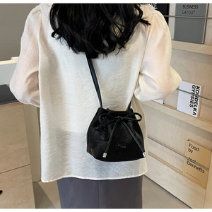 Détail d'un sac seau noir en cuir avec nœud, porté par un mannequin dans un décor épuré