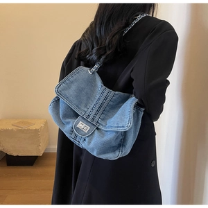 Detail of blue denim tote bag featuring silver chain strap and metal swivel lock closure