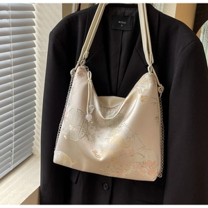 Macro detail of refined floral embroidery and leather strap on beige silk hobo bag