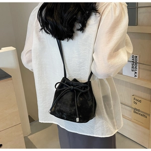 Détail d'un sac seau en cuir noir mat avec cordon à nœud porté par un mannequin femme