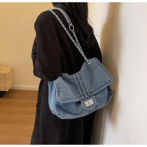 Detail of blue washed denim bag with silver chain strap and metal swivel lock closure