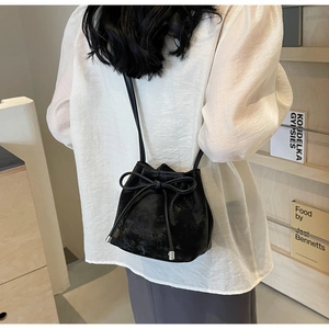 Détail du sac seau noir en cuir avec cordon de serrage, nœud et embouts argentés