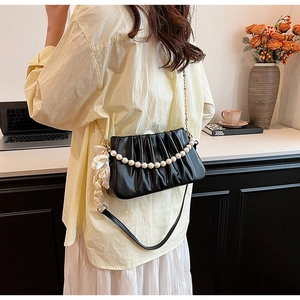 Detail of black pleated cloud bag featuring pearl chain and white silk bow charm
