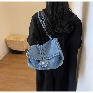 Detail of blue denim tote bag featuring silver metal chain strap on a model shoulder