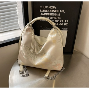Detail of beige satin bag with floral embroidery and elegant pearl zipper charm
