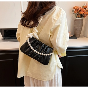 Detail of black pleated shoulder bag with pearl handle and white silk bow accent