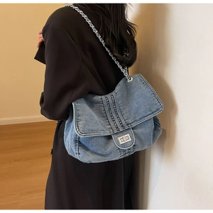 Detailed close-up of blue denim flap bag with metal chain strap and turn-lock buckle