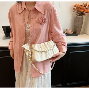 Detail of white pleated shoulder bag featuring pearl chains and a silk ribbon bow