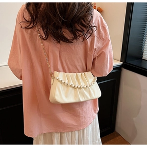 Detail of cream pleated cloud bag with pearl handle and gold chain strap on model