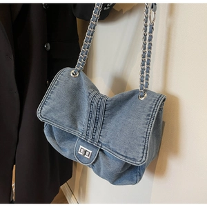 Detail of washed denim shoulder bag featuring silver chain strap and metal turn-lock closure