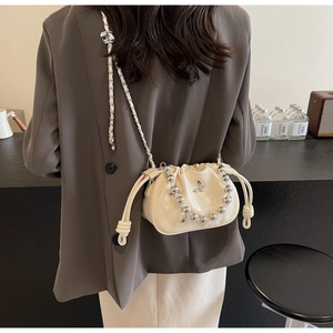 Detail of a creamy white pleated drawstring bucket bag with silver beaded chain and charm