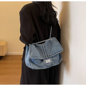 Model wearing a washed denim tote bag with chain strap and silver twist lock over a black coat