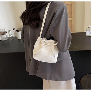 Détail d'un sac seau blanc crème avec nœud de serrage sur un mannequin dans un café