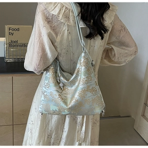 Detailed embroidery on a cream silk crossbody tote bag shown in a soft lifestyle setting