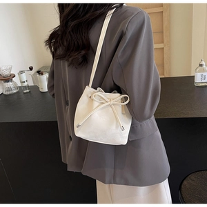 Sac seau blanc avec cordon à nœud porté par un mannequin dans un décor de café chic