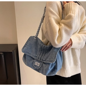 Detail of blue denim tote bag featuring silver chain strap and quilted texture on a white sweater
