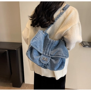 Detail of light blue denim shoulder bag with metal chain strap on model shoulder