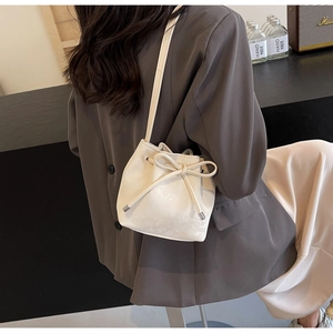 Détail du sac seau blanc à cordon avec nœud porté par un mannequin en blazer brun
