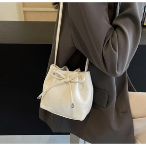 Gros plan d'un sac seau blanc crème avec cordon et nœud élégant porté par un modèle