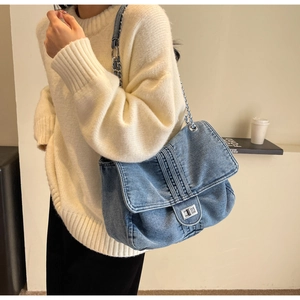 Detail of light blue washed denim shoulder bag with chain strap and metal lock buckle