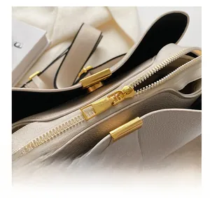 Detailed close-up of smooth gold zipper and lychee pattern leather on beige bucket bag