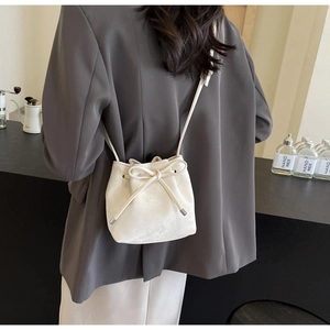 Modèle portant un sac seau beige minimaliste avec nœud coulissant et bandoulière fine