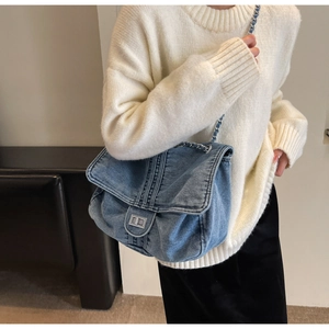 Detail of blue denim chain bag featuring a silver metal lock and woven leather strap