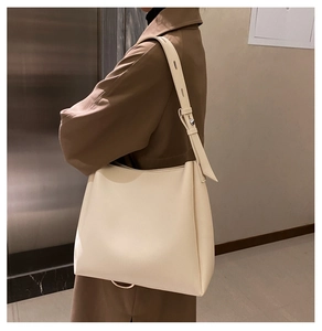 Close-up of off-white leather tote bag showing adjustable shoulder strap with round metal buckle