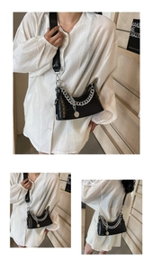 Detail of black crocodile texture shoulder bag with silver chain and coin pendant