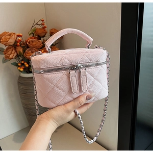 Pink quilted leather mini vanity bag with chain strap held by a hand in a home setting